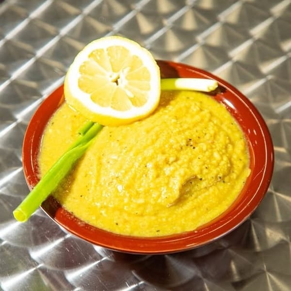 Bright yellow dip in a red bowl, garnished with a lemon slice and green onions.