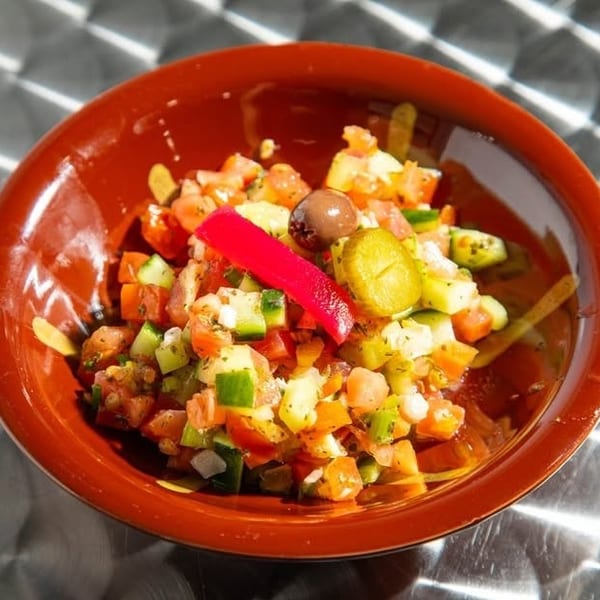 Diced tomato and cucumber salad with olives and red pepper in a brown bowl.
