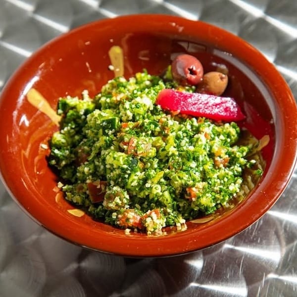 A vibrant tabbouleh salad in a brown bowl, garnished with olives and a red pepper slice.