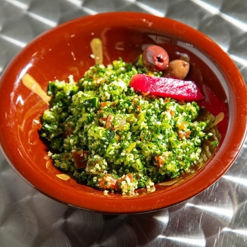 A vibrant tabbouleh salad in a brown bowl, garnished with olives and a red pepper slice.