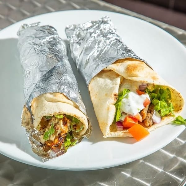 Two shawarma wraps on a white plate, one partially unwrapped showing meat, lettuce, tomato, and sauce.