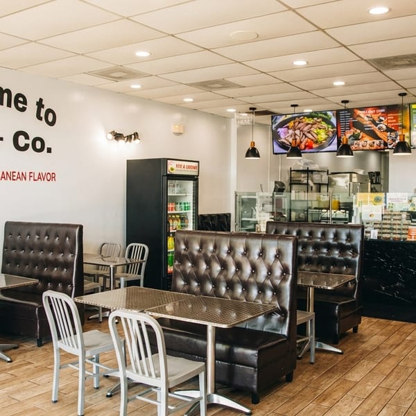 Bright Pita & Co. restaurant interior with brown booths, metal tables, and a counter with menu screens.